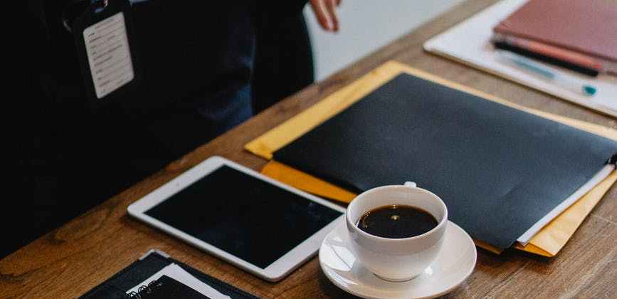 businessperson standing near table with cup of coffee and folders